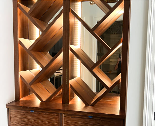 Wooden wine rack with diagonal shelves forming a geometric pattern, set against a mirrored back panel with built-in lighting.