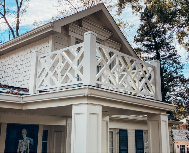 Two-story house with white Chippendale-style balcony railing; a skeleton decoration is visible in a window below.