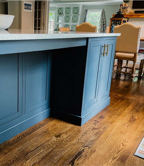 Blue kitchen island with gold handles on a wood floor, with upholstered chairs and cabinetry visible in the background.