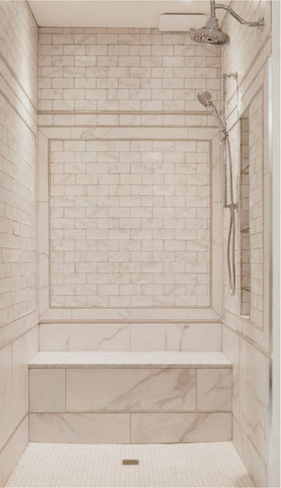 A tiled shower with a built-in bench, overhead and handheld showerheads, and a framed tile design on the back wall.