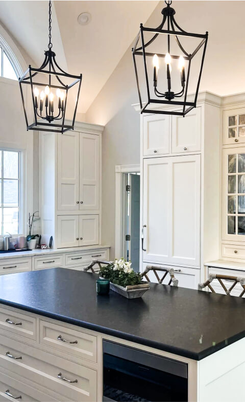 Modern kitchen with white cabinets, black countertop island, two large black lantern pendant lights, and a small plant centerpiece.