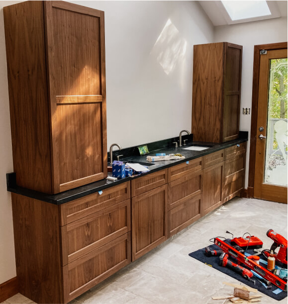 A kitchen under construction with wooden cabinets, black countertops, tools, and materials scattered on a mat on the floor.