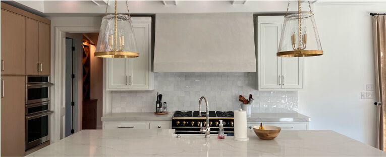 Modern kitchen with a marble island, double ovens, a gas stove, white cabinets, and two gold pendant lights hanging above the countertop.