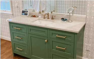 Green bathroom vanity with gold hardware, a white countertop, sink, mirror, small display screen, and a round makeup mirror on the right.