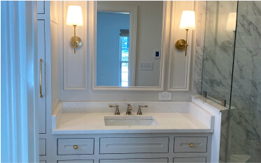 Bathroom vanity with a rectangular sink, marble countertop, mirror, two wall sconces, and glass shower enclosure on the right.